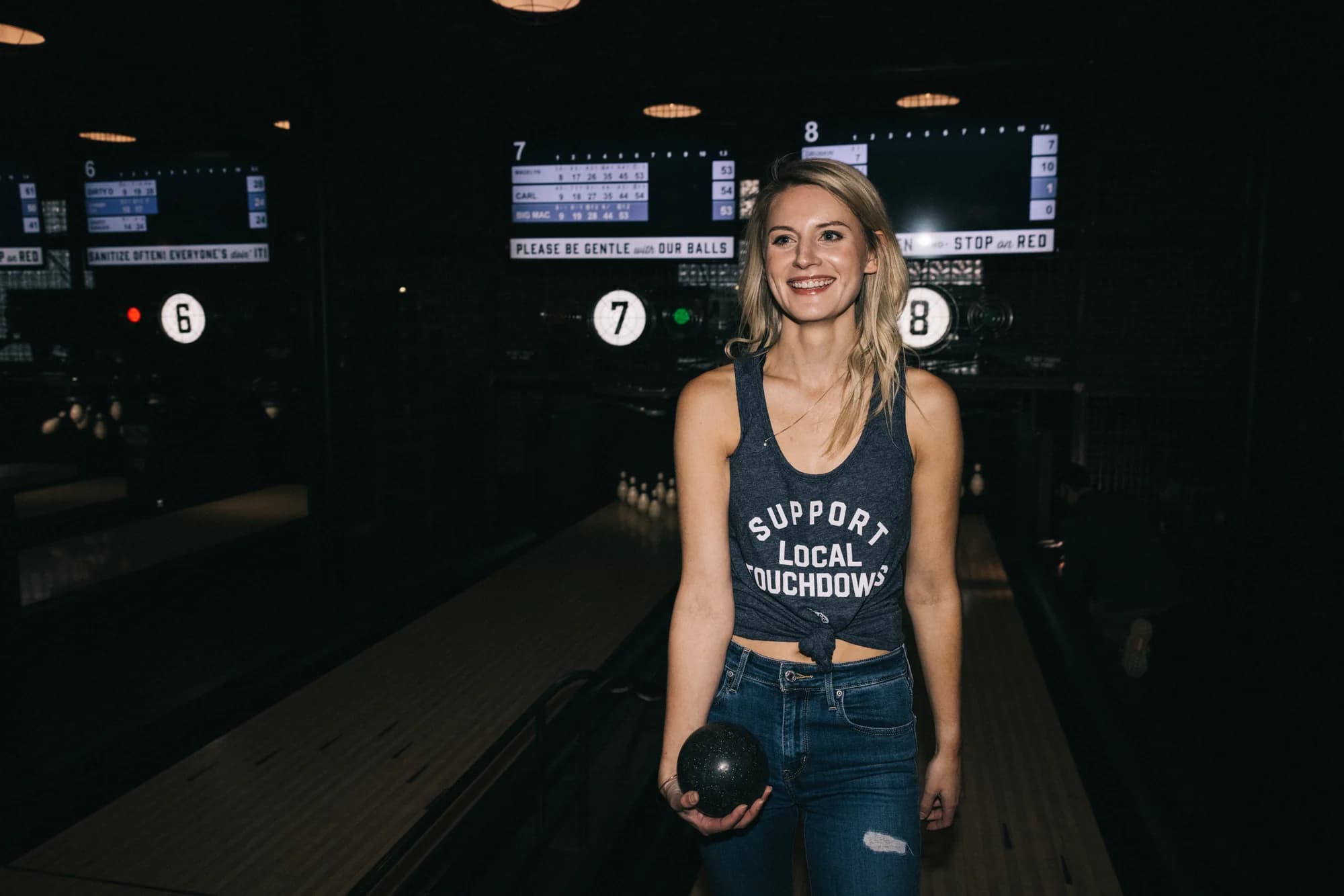A woman in the Support Local Touchdowns tank at a bowling lane